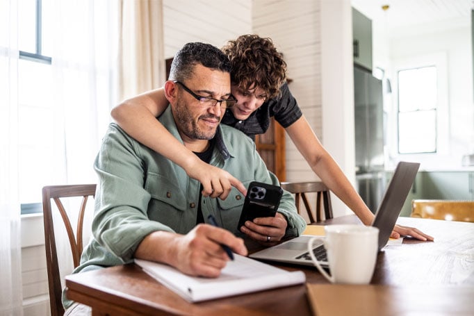 Woman has arm around man and pointing at his phone