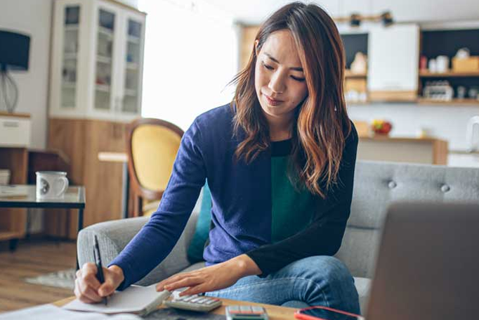 Woman sitting on couch, writing on paper