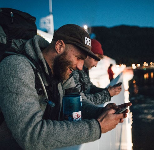 Two men looking at their cell phones while leaning on a bridge